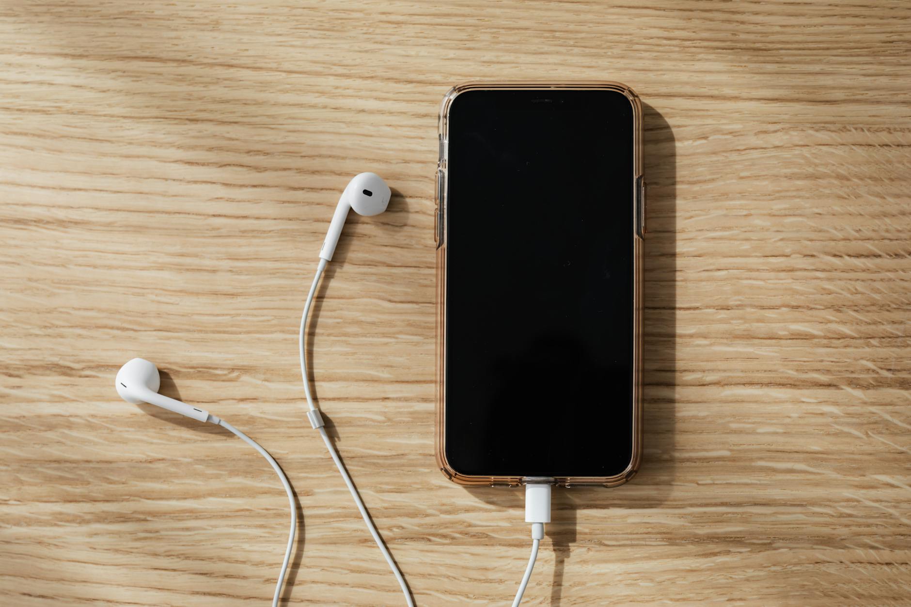 charging smartphone and white earphones on wooden table